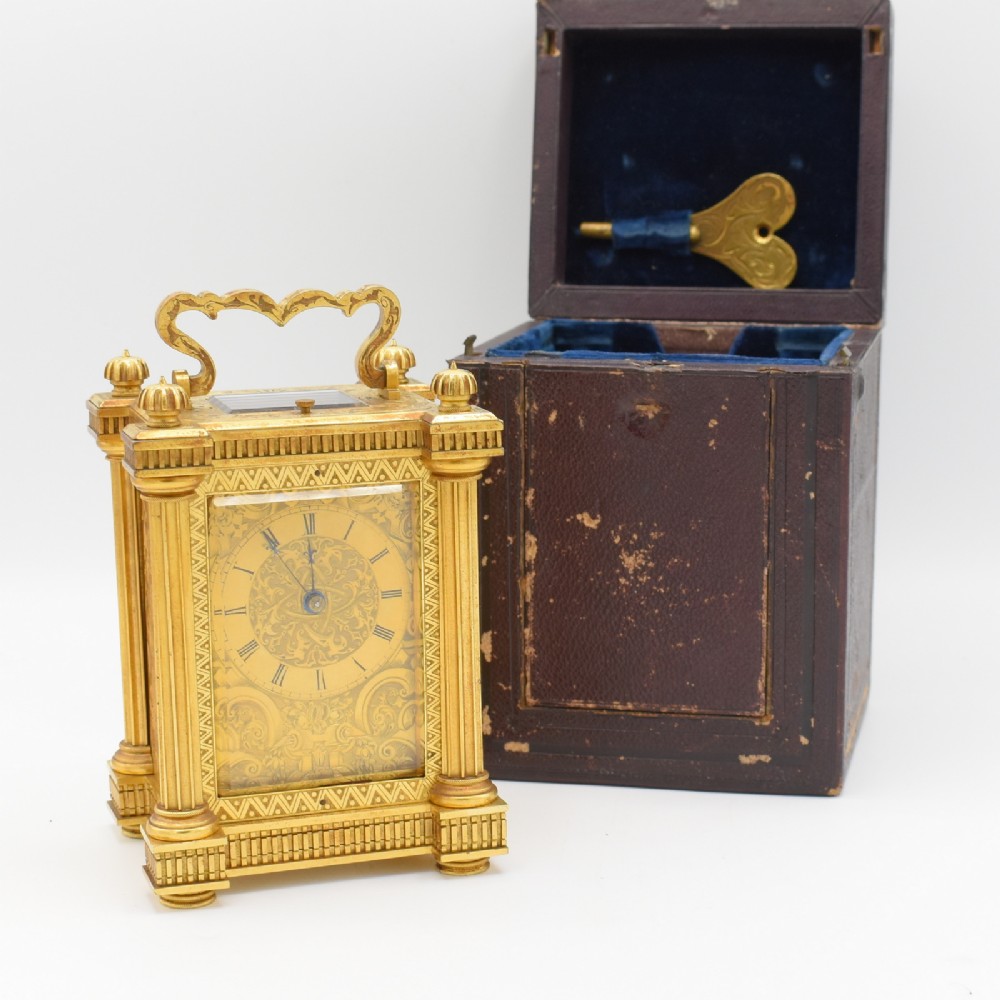 An ornate gilt brass repeating carriage clock featuring fluted corner columns alongside its original leather transport case and key.