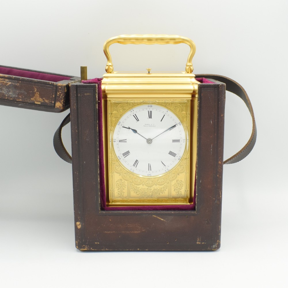 An antique gilt brass carriage clock with an engraved face and white enamel dial housed inside a fitted dark brown leather travelling case with a handle. View II