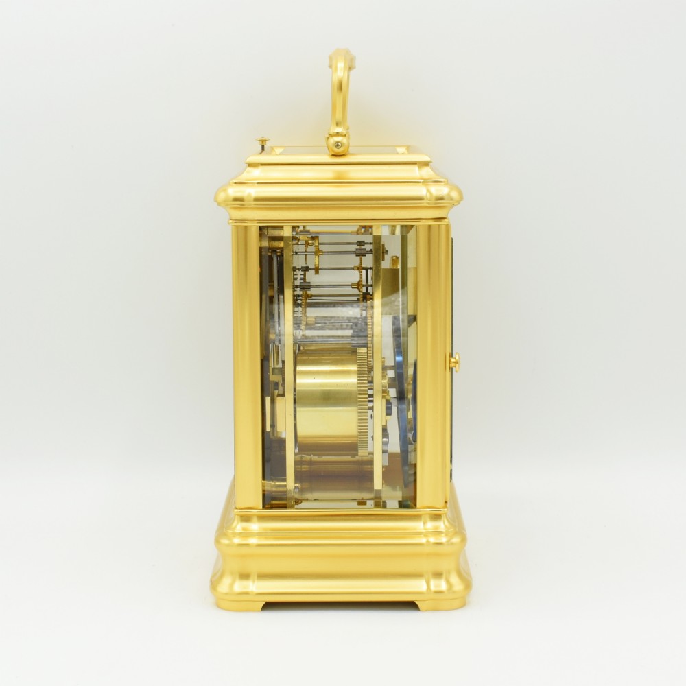An antique gilt brass carriage clock with an engraved face and white enamel dial housed inside a fitted dark brown leather travelling case with a handle. View V