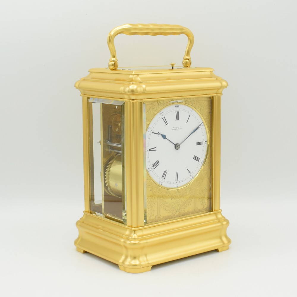An antique gilt brass carriage clock with an engraved face and white enamel dial housed inside a fitted dark brown leather travelling case with a handle. View VII