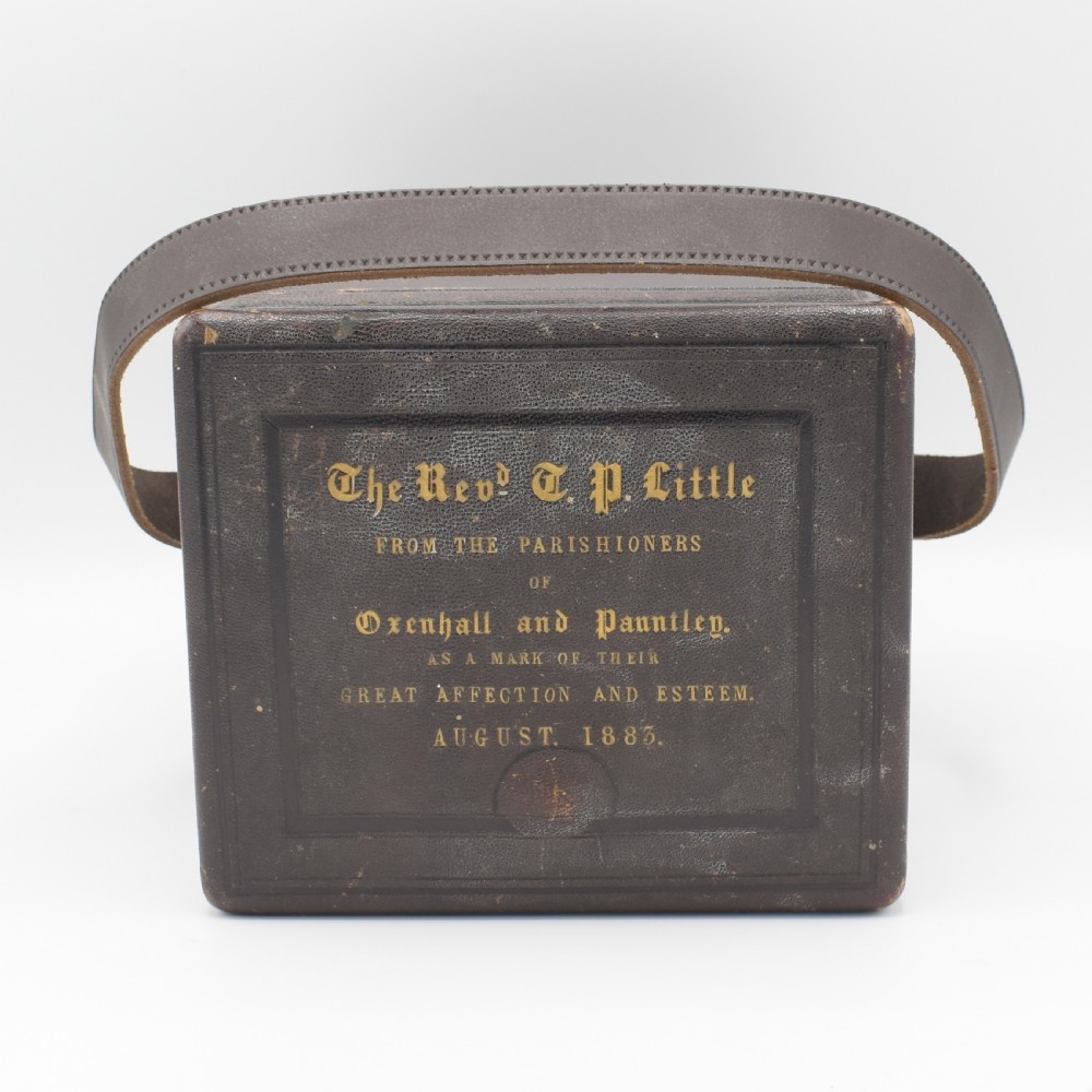 An antique gilt brass carriage clock with an engraved face and white enamel dial housed inside a fitted dark brown leather travelling case with a handle. View IX