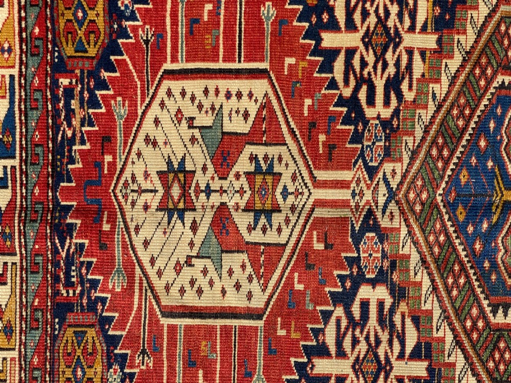An antique hand-knotted Caucasian Shirvan wool rug featuring central geometric diamond medallions and intricate layered borders in red, cream, and navy blue. View II