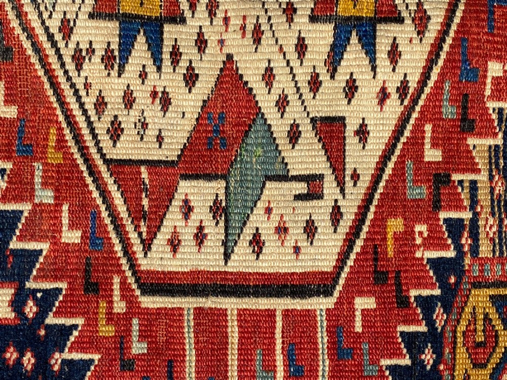 An antique hand-knotted Caucasian Shirvan wool rug featuring central geometric diamond medallions and intricate layered borders in red, cream, and navy blue. View V