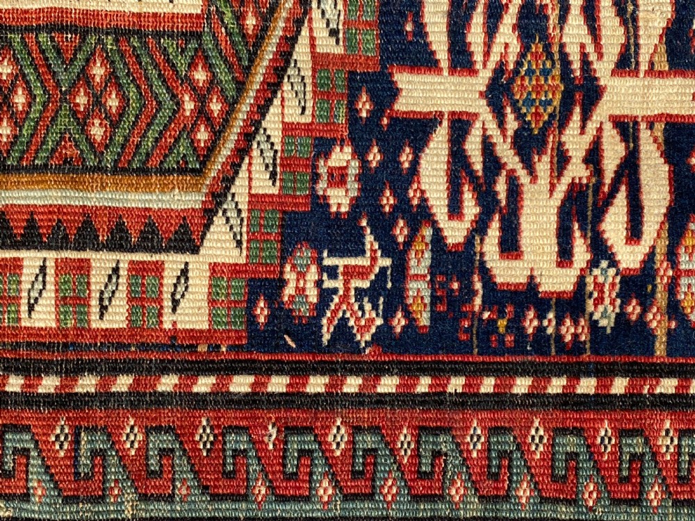 An antique hand-knotted Caucasian Shirvan wool rug featuring central geometric diamond medallions and intricate layered borders in red, cream, and navy blue. View VI