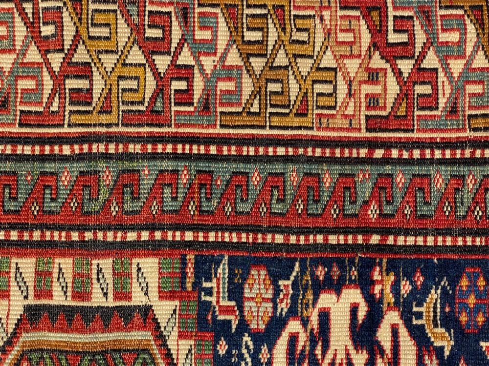An antique hand-knotted Caucasian Shirvan wool rug featuring central geometric diamond medallions and intricate layered borders in red, cream, and navy blue. View VII