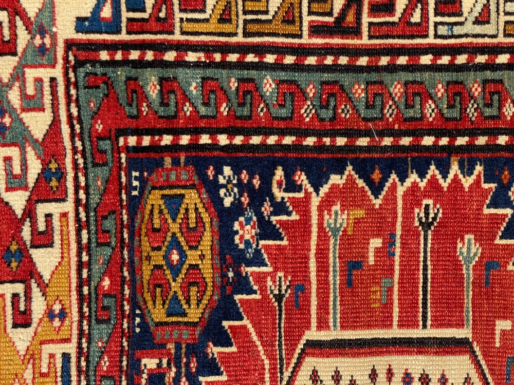 An antique hand-knotted Caucasian Shirvan wool rug featuring central geometric diamond medallions and intricate layered borders in red, cream, and navy blue. View VIII