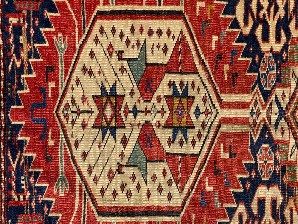 An antique hand-knotted Caucasian Shirvan wool rug featuring central geometric diamond medallions and intricate layered borders in red, cream, and navy blue. View IX