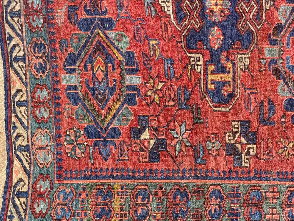 An antique Caucasian Soumak wool rug featuring geometric stepped medallions on a terracotta red field with blue and multi-coloured borders. View II