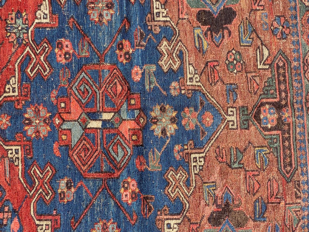An antique Caucasian Soumak wool rug featuring geometric stepped medallions on a terracotta red field with blue and multi-coloured borders. View VIII
