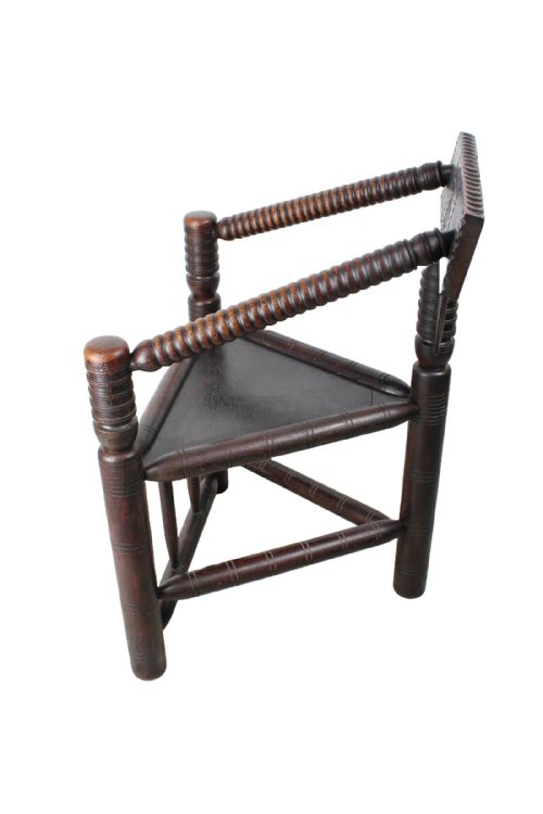 fig 1. An antique dark brown oak turners chair featuring a triangular seat, bobbin-turned legs and arms, and a carved geometric back crest panel.