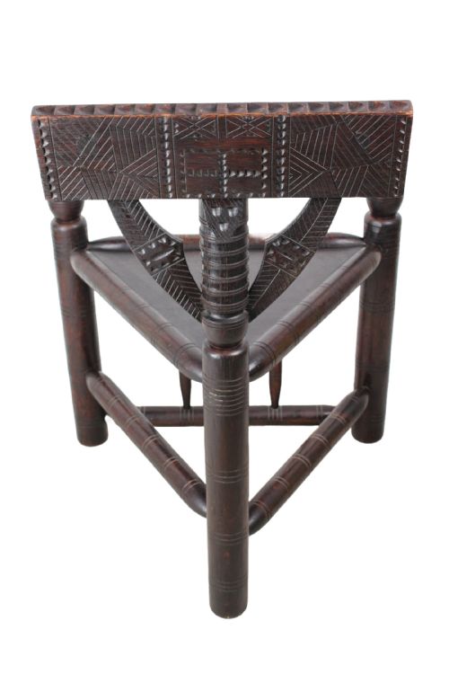 fig 2. An antique dark brown oak turners chair featuring a triangular seat, bobbin-turned legs and arms, and a carved geometric back crest panel.
