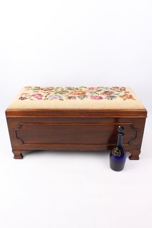fig 1. A low rectangular dark mahogany storage ottoman featuring a beige upholstered top with floral needlework embroidery.