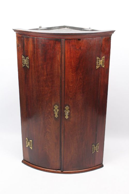 fig 1. A Georgian mahogany bow front corner cupboard with twin curved doors and decorative brass hinges and keyhole escutcheons.
