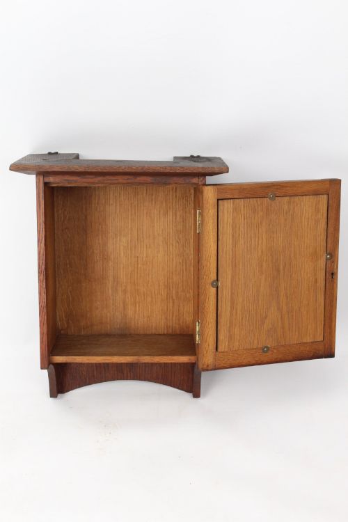 fig 1. A small Edwardian Arts and Crafts oak wall cabinet featuring a single door decorated with a carved stylized floral panel and small brass hinges.