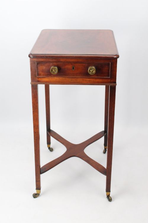 fig 1. A small Georgian mahogany side table featuring a single drawer with brass ring handles, square tapered legs joined by an X-form stretcher, and brass castors.