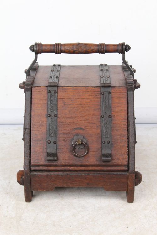 fig 1. A Victorian Gothic Revival dark oak coal scuttle featuring sloped timber lids, a turned handle, and black wrought iron scrollwork straps.