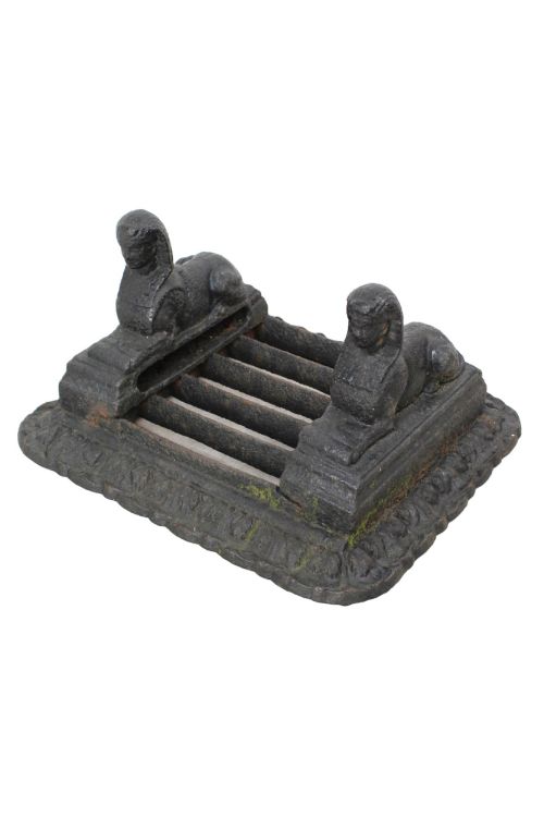 fig 1. A dark cast iron boot scraper featuring twin sphinx figures flanking a central slatted grate set upon a decorative moulded base.