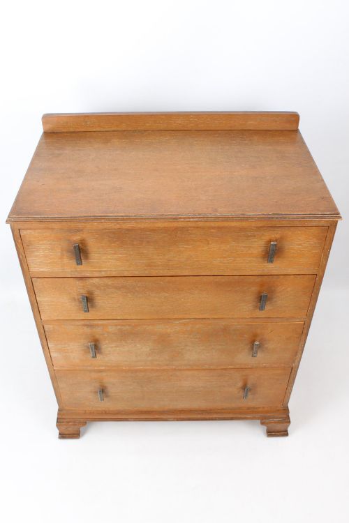 fig 1. A light oak Art Deco chest of drawers featuring four drawers with textured metal handles, a low gallery back, and bracket feet.