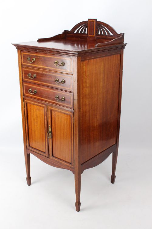 fig 1. An Edwardian mahogany music cabinet featuring inlaid stringing, three top drawers with brass handles, a two-door lower cupboard, and a carved cresting gallery.
