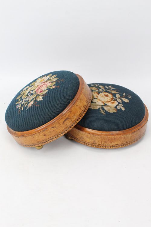 fig 1. A pair of circular Early Victorian footstools featuring teal floral needlepoint tops within light wood frames and geometric mosaic borders.