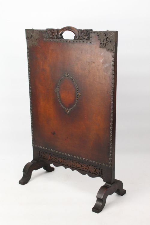 fig 1. An Edwardian Arts and Crafts fire screen constructed from carved oak and warm brown leather featuring brass studwork and a central oval motif.