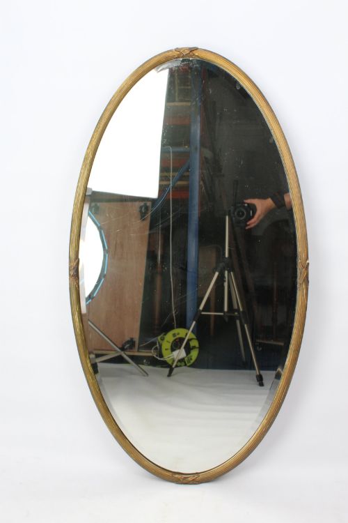 fig 1. A large Victorian oval wall mirror featuring a gilded reeded frame with decorative cross-ribbon accents at four points.