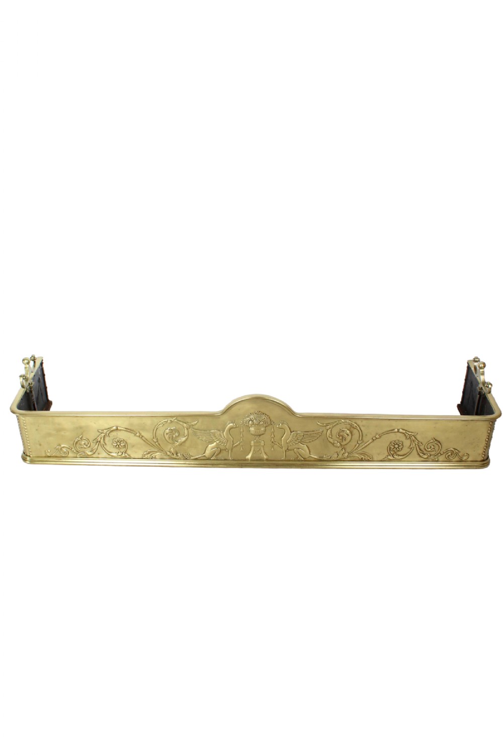 A large Victorian brass fire fender with embossed Neoclassical relief depicting winged griffins, a central urn, and scrolling foliage.