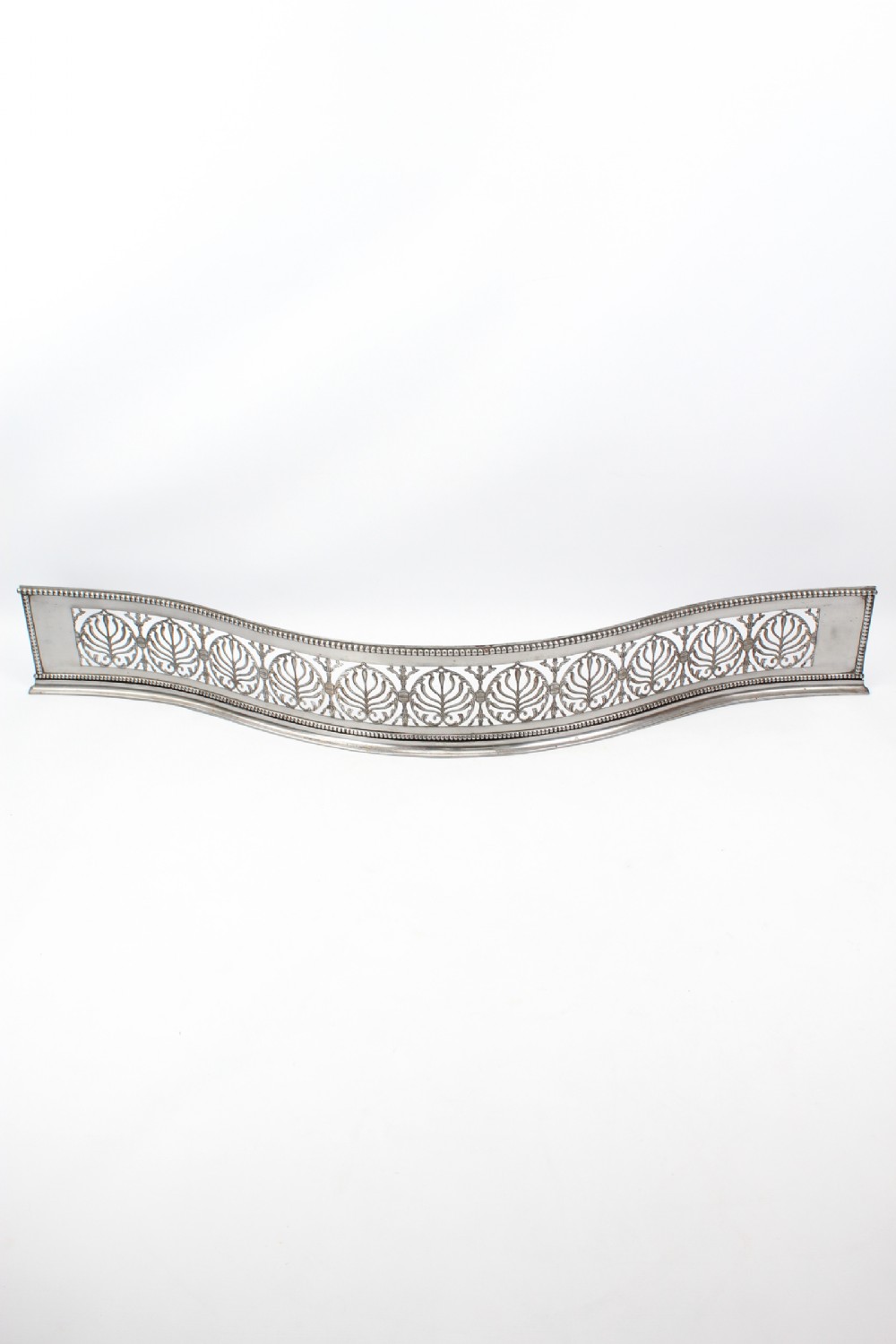 A broad Georgian steel fire fender with a serpentine front and pierced foliate engraving.