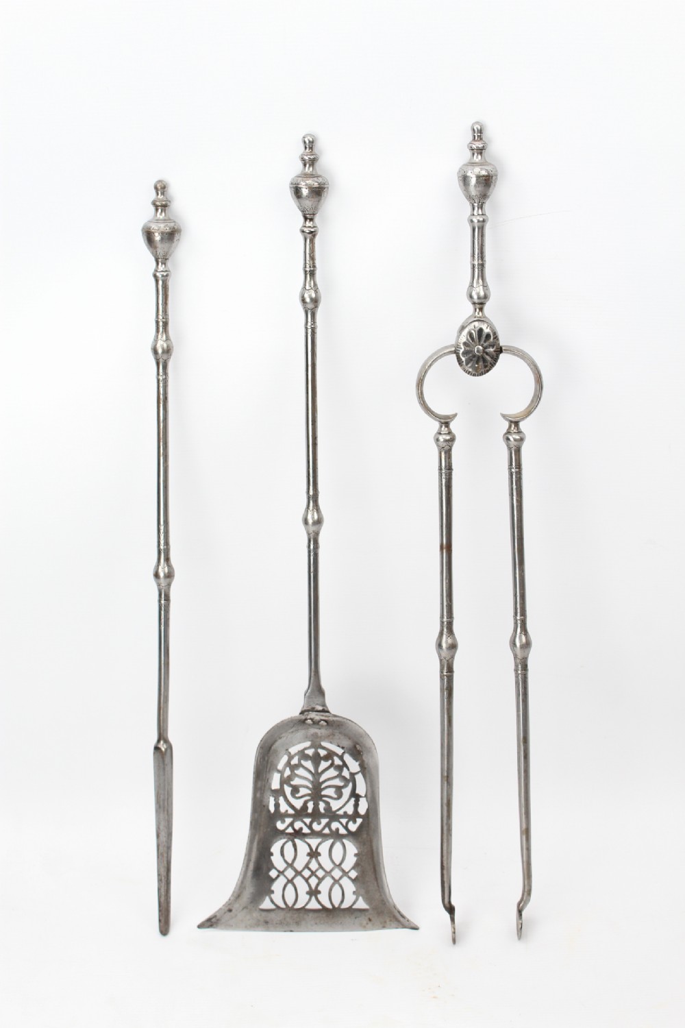 A three-piece set of Georgian polished steel fire tools comprising a poker, a pierced shovel, and tongs with turned urn finials.