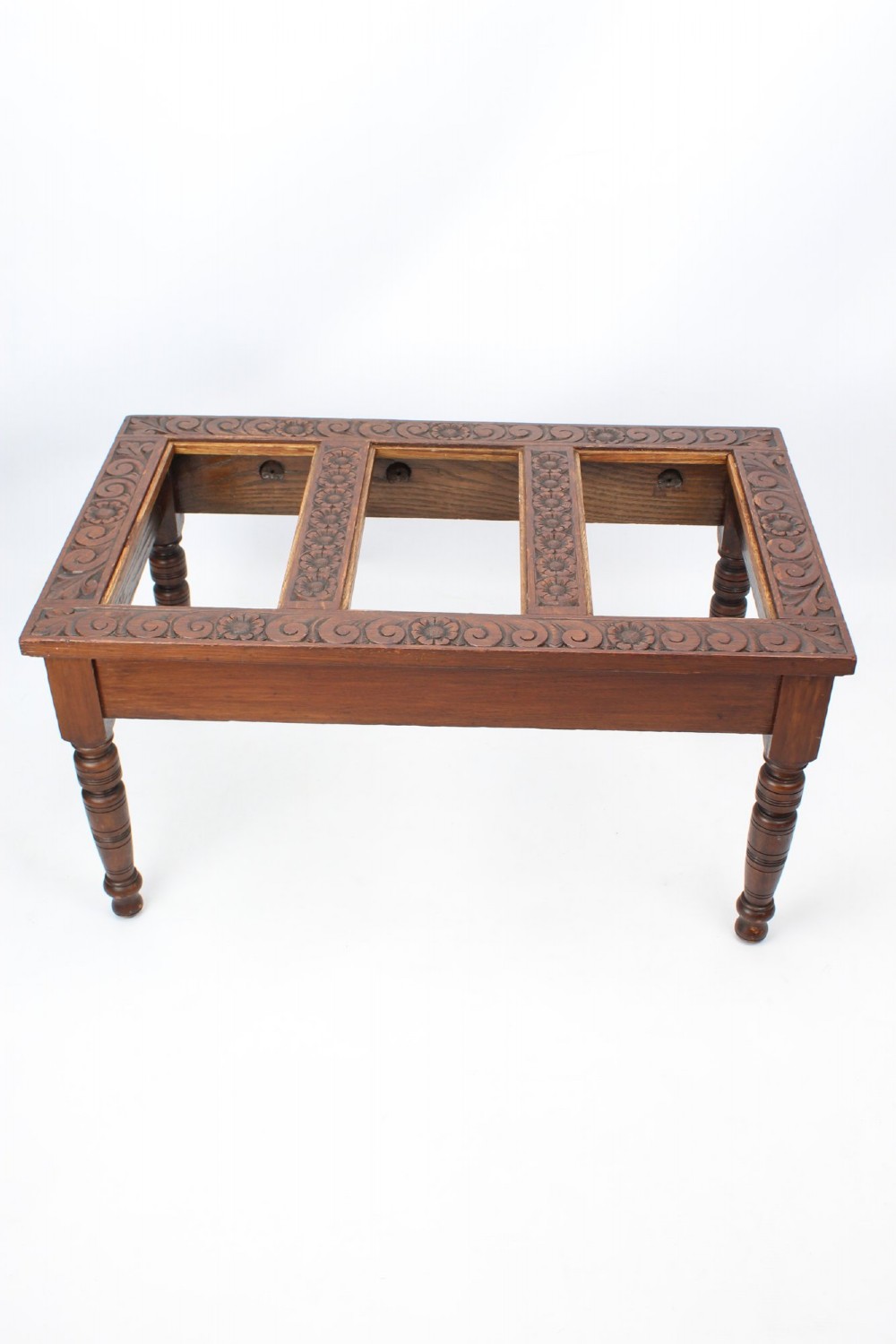 An Edwardian carved oak luggage stand with relief floral carving along the open top frame and turned wooden legs.