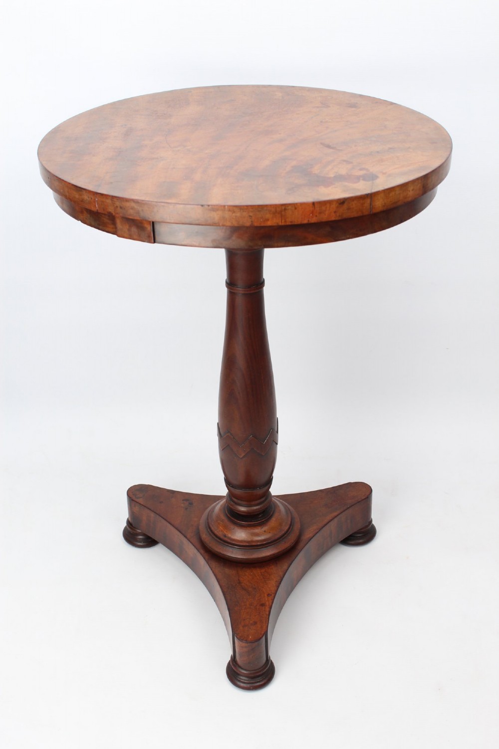 A circular mahogany wine table from the William IV period featuring a turned central column on a triform base with flattened bun feet.