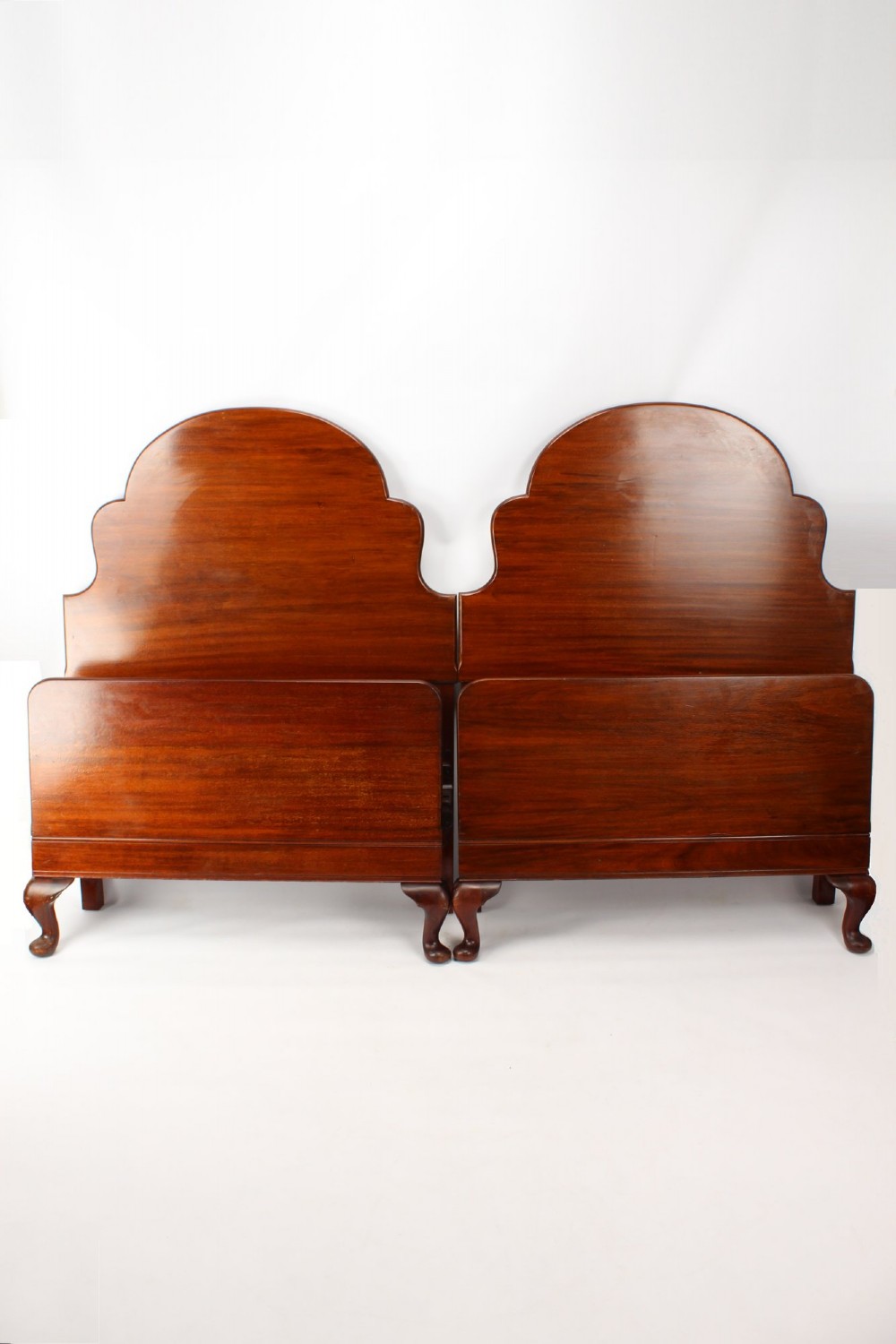 A matching pair of Art Deco mahogany single beds with stepped, arched headboards and low footboards on short cabriole feet.