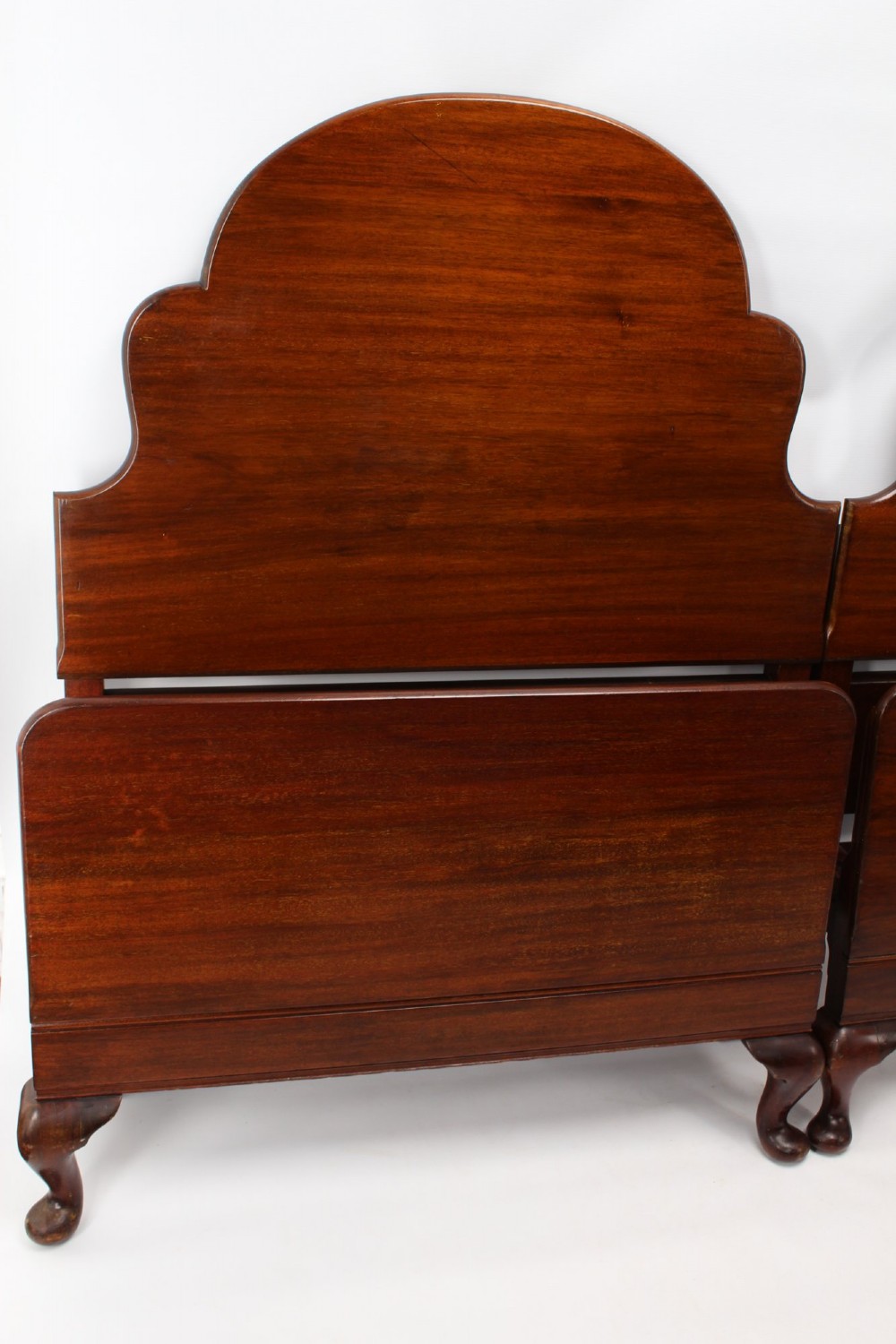 A matching pair of Art Deco mahogany single beds with stepped, arched headboards and low footboards on short cabriole feet. View II