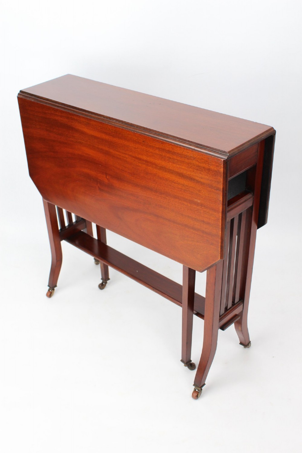A compact Edwardian mahogany Sutherland table with folded side leaves, slatted end supports, and legs fitted with brass castors.