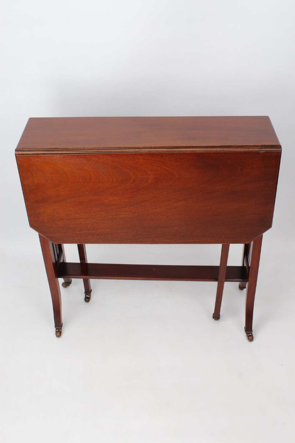 A compact Edwardian mahogany Sutherland table with folded side leaves, slatted end supports, and legs fitted with brass castors. View III