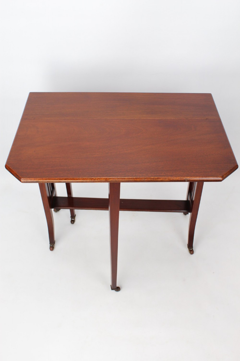 A compact Edwardian mahogany Sutherland table with folded side leaves, slatted end supports, and legs fitted with brass castors. View IV