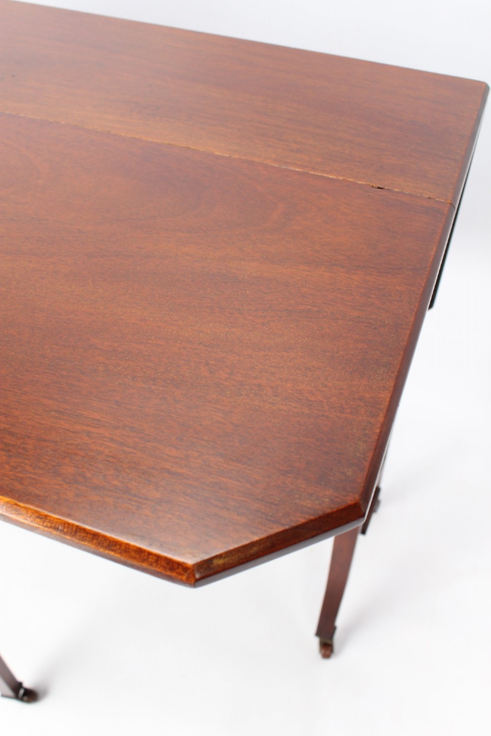 A compact Edwardian mahogany Sutherland table with folded side leaves, slatted end supports, and legs fitted with brass castors. View VI