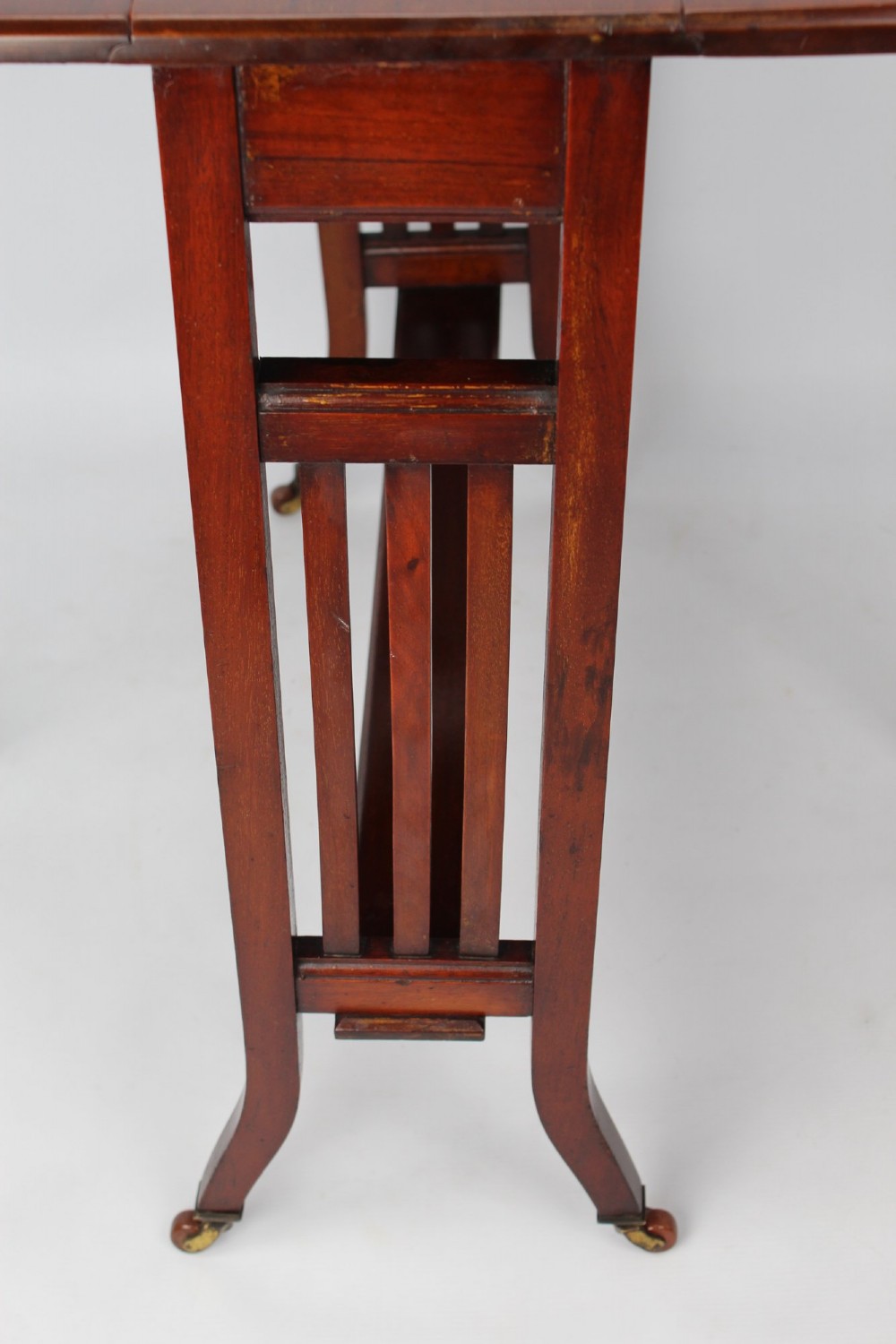 A compact Edwardian mahogany Sutherland table with folded side leaves, slatted end supports, and legs fitted with brass castors. View IX