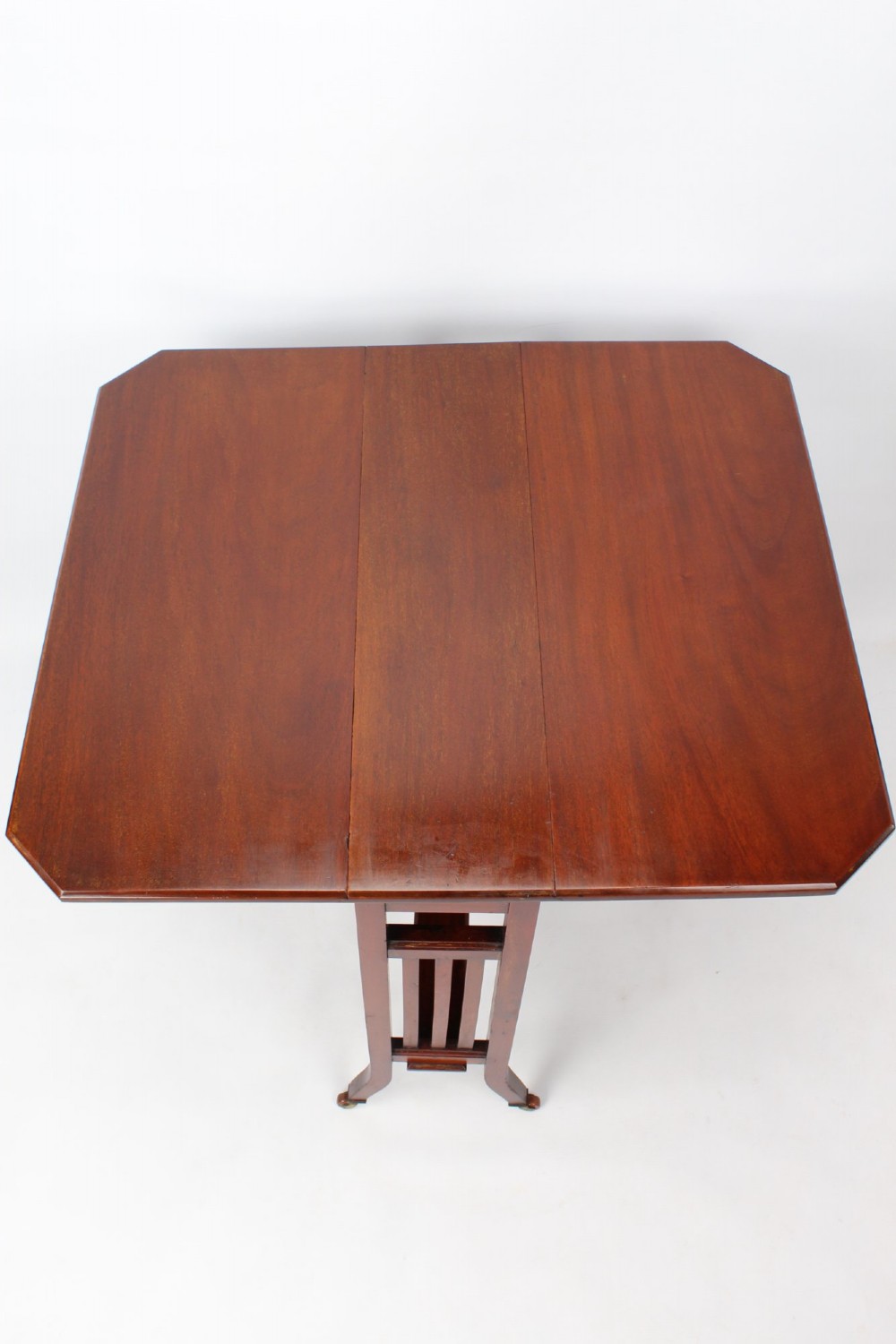 A compact Edwardian mahogany Sutherland table with folded side leaves, slatted end supports, and legs fitted with brass castors. View X