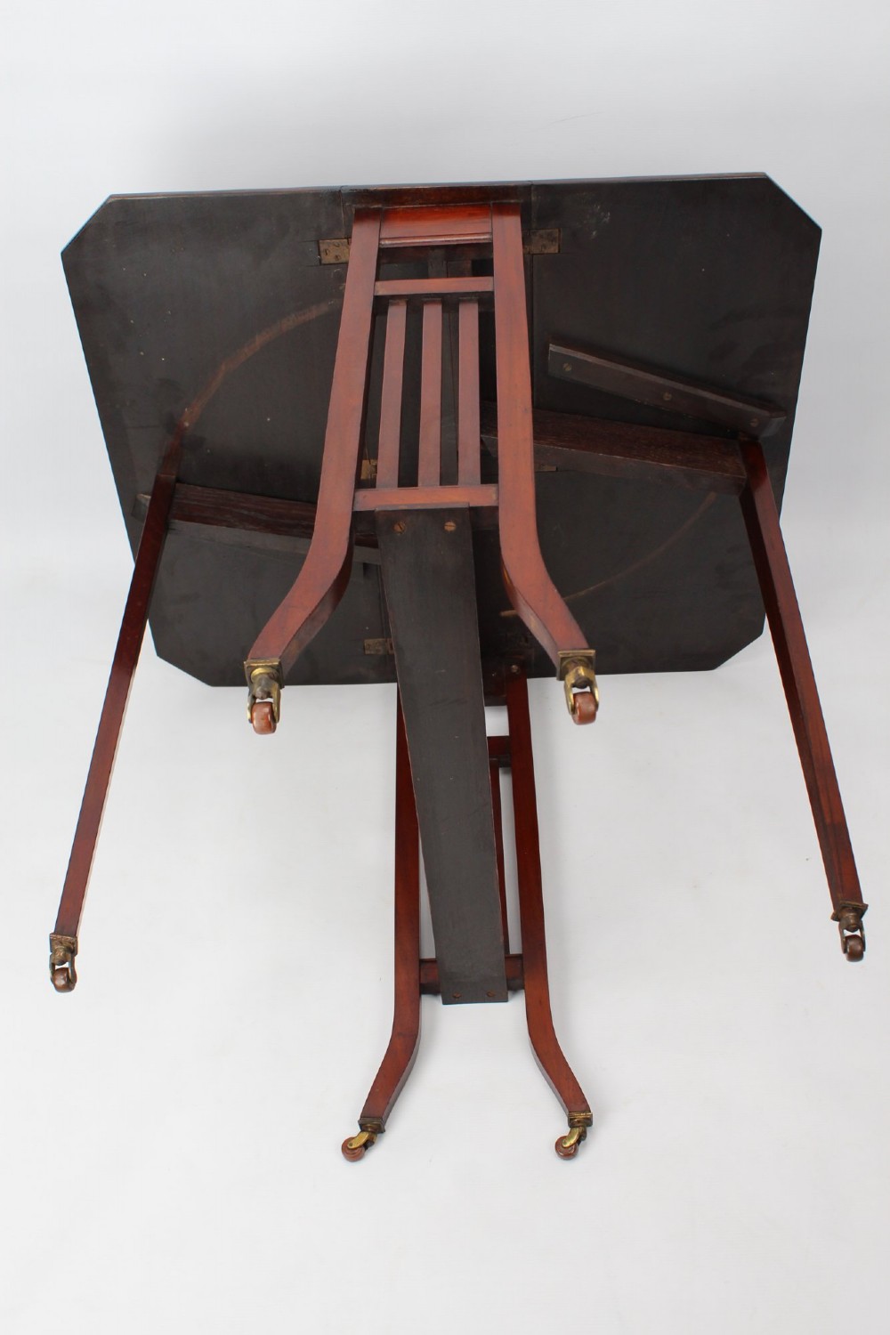 A compact Edwardian mahogany Sutherland table with folded side leaves, slatted end supports, and legs fitted with brass castors. View XII