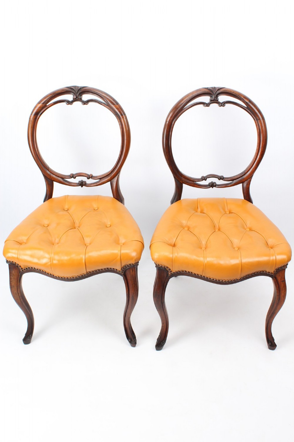 A pair of Victorian rosewood balloon back side chairs featuring button-tufted tan leather upholstery and cabriole front legs.