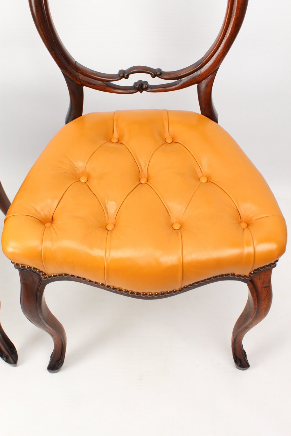 A pair of Victorian rosewood balloon back side chairs featuring button-tufted tan leather upholstery and cabriole front legs. View VI