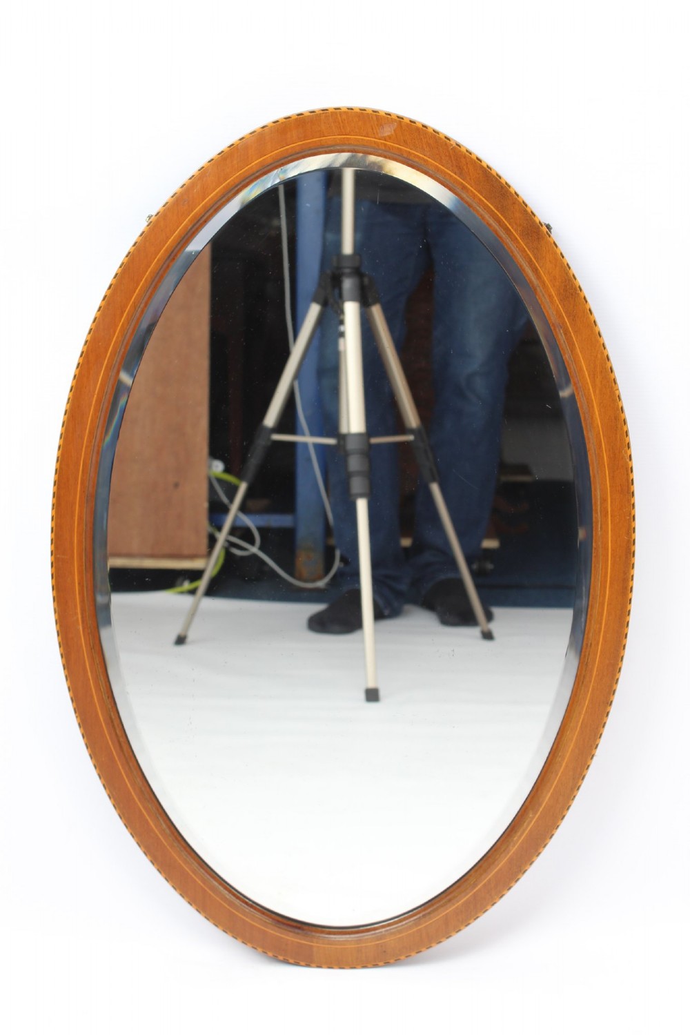 An oval wall mirror framed in warm mahogany timber with geometric chequered inlay along the outer border. View II