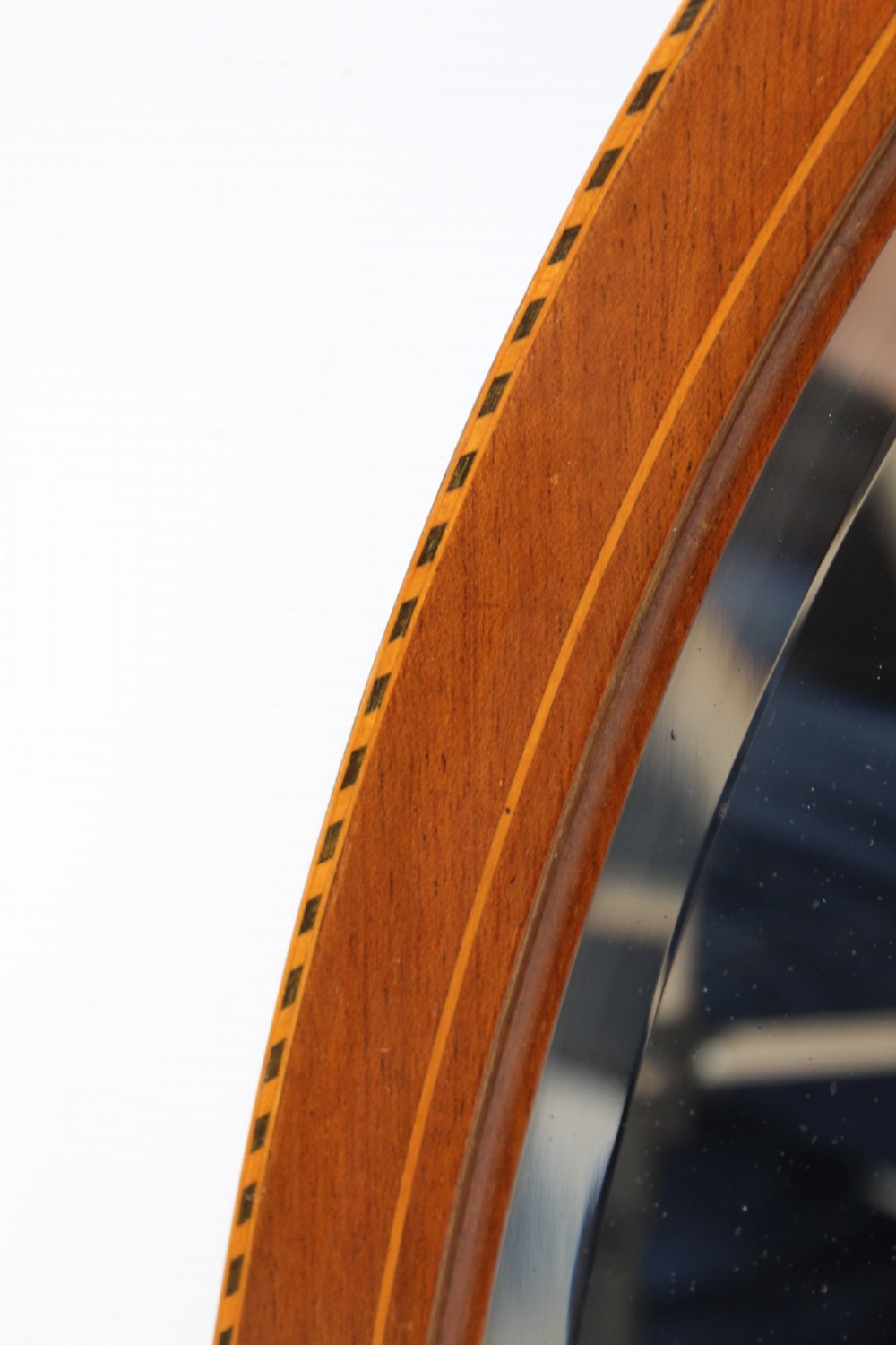 An oval wall mirror framed in warm mahogany timber with geometric chequered inlay along the outer border. View III