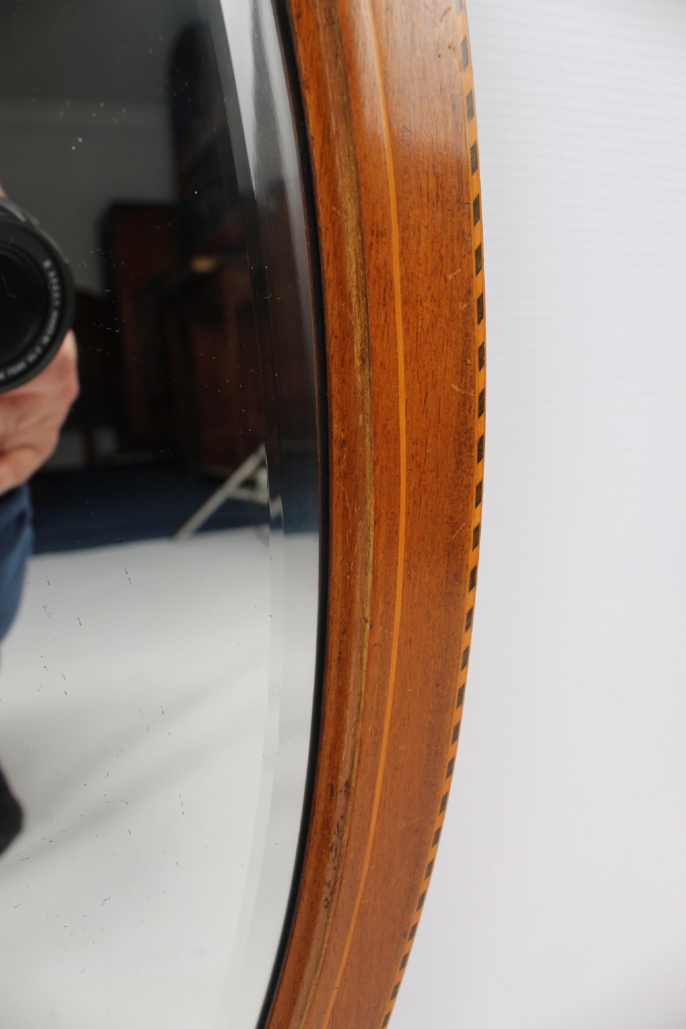 An oval wall mirror framed in warm mahogany timber with geometric chequered inlay along the outer border. View V