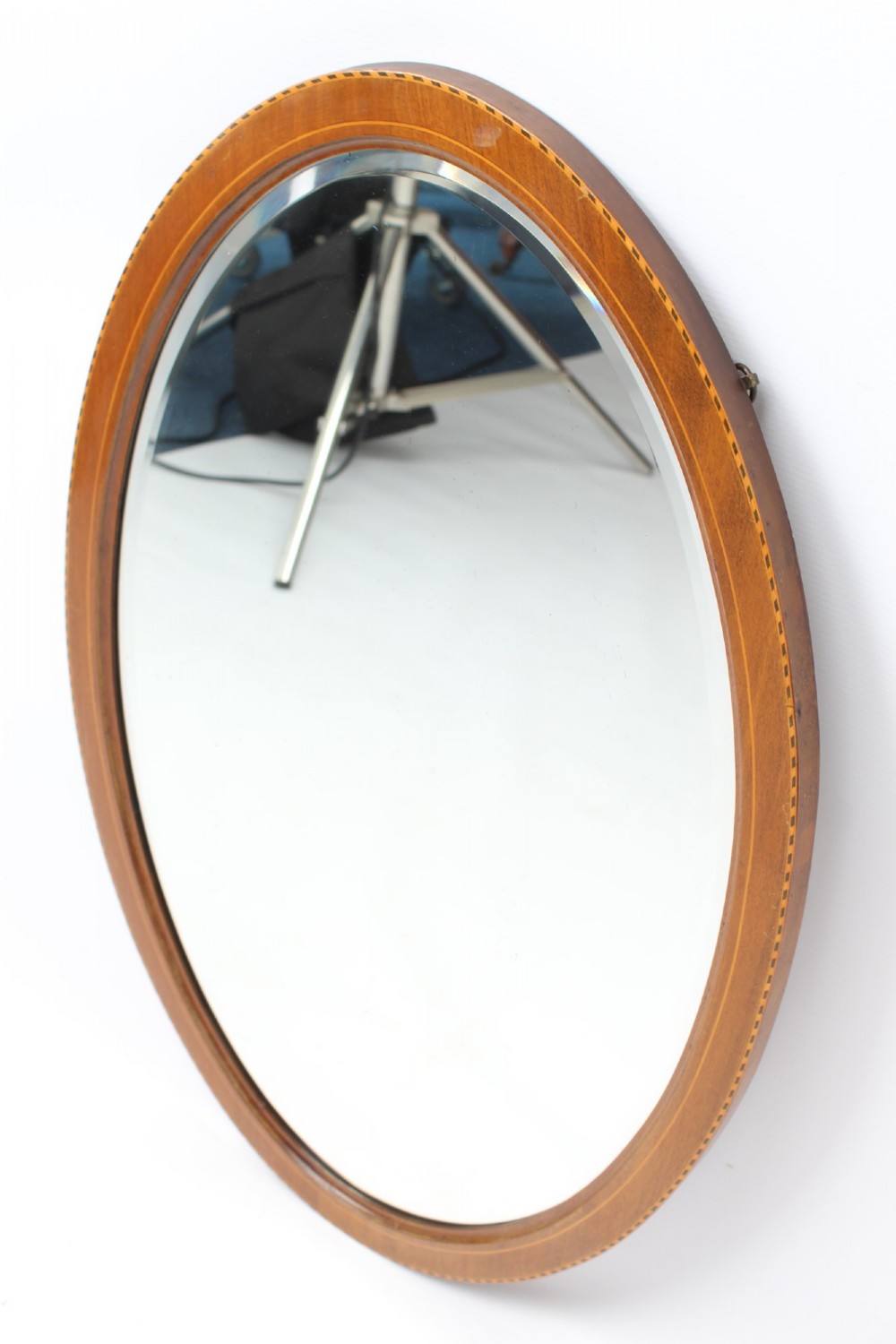 An oval wall mirror framed in warm mahogany timber with geometric chequered inlay along the outer border. View VIII