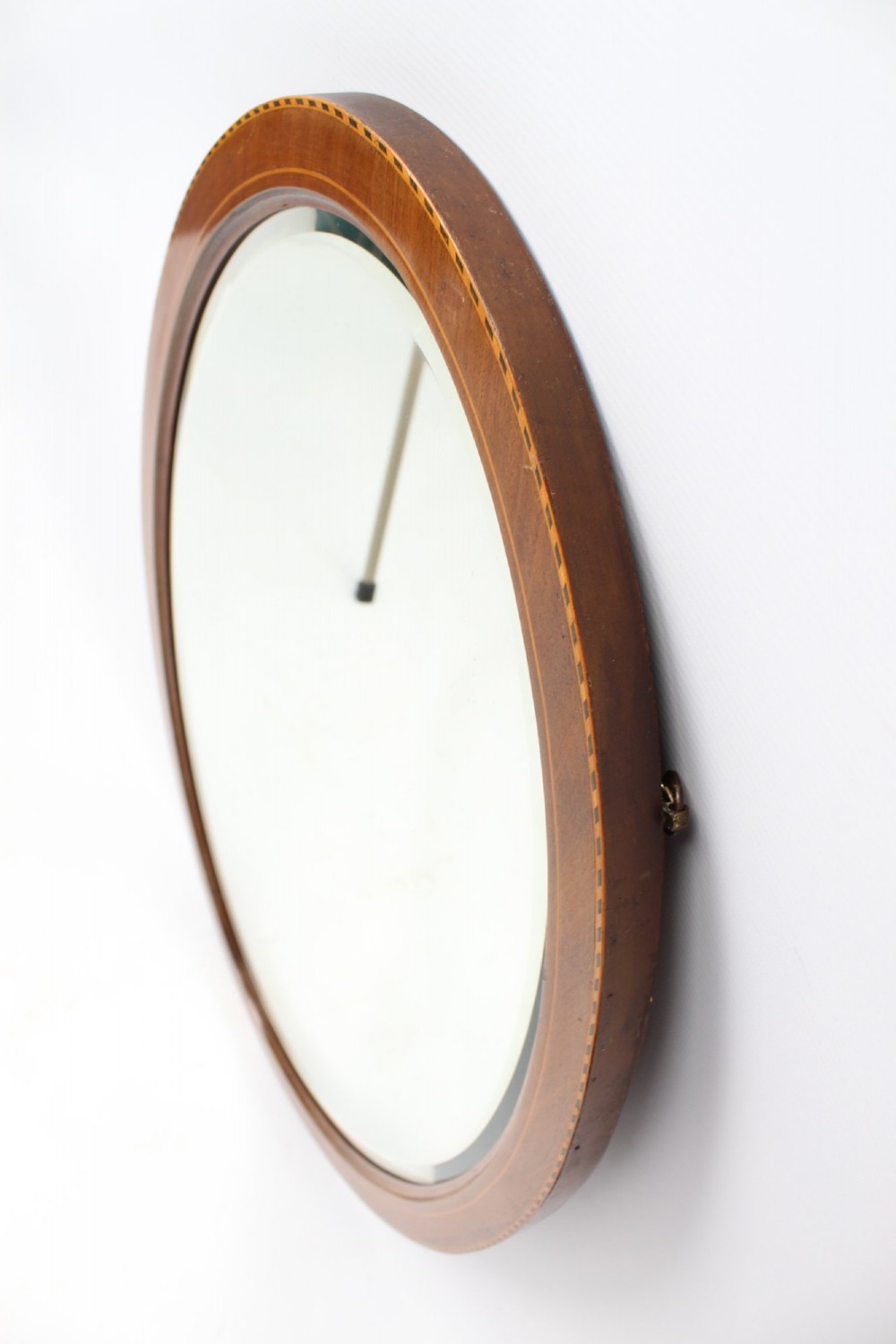 An oval wall mirror framed in warm mahogany timber with geometric chequered inlay along the outer border. View IX