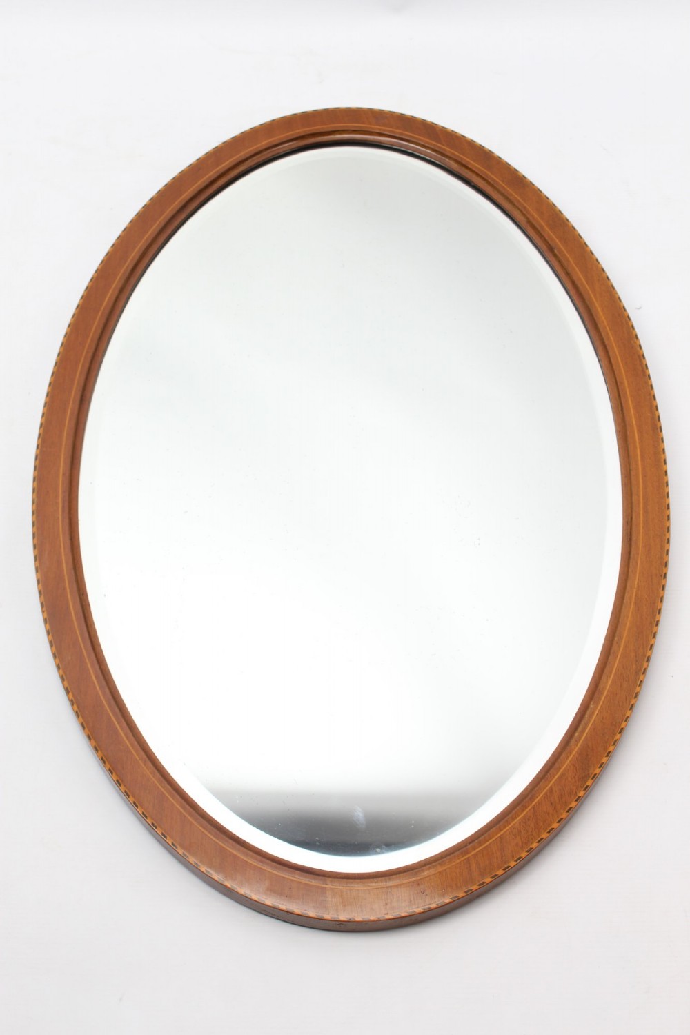 An oval wall mirror framed in warm mahogany timber with geometric chequered inlay along the outer border. View X