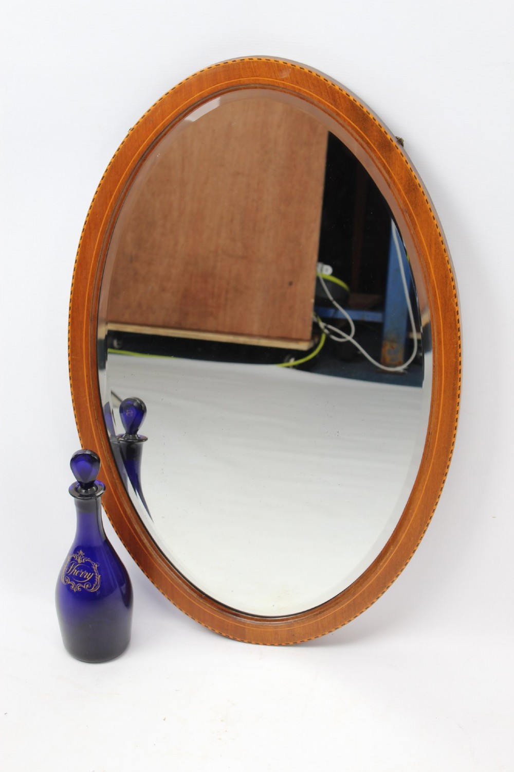 An oval wall mirror framed in warm mahogany timber with geometric chequered inlay along the outer border. View XI