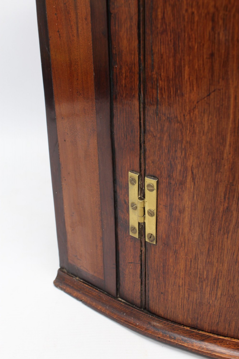A Georgian oak bow-front corner cupboard with twin doors, exposed brass H-hinges, crossbanded veneer borders, and central brass escutcheons. View XI
